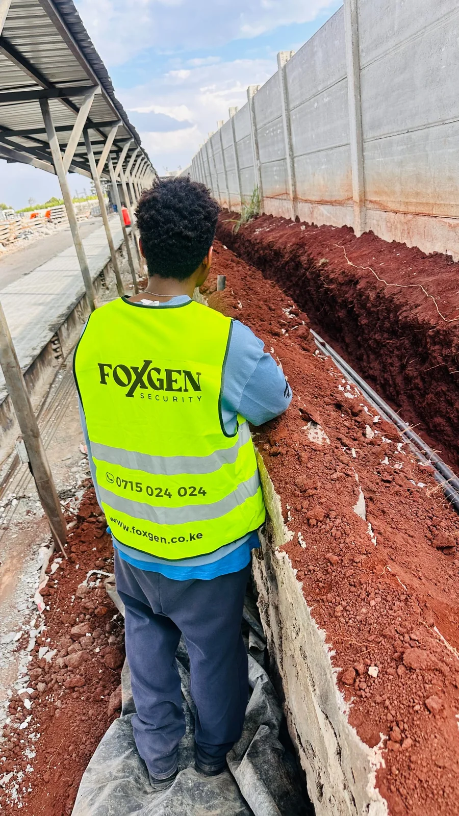 Foxgen technician beside conduits in an open trench along a boundary wall