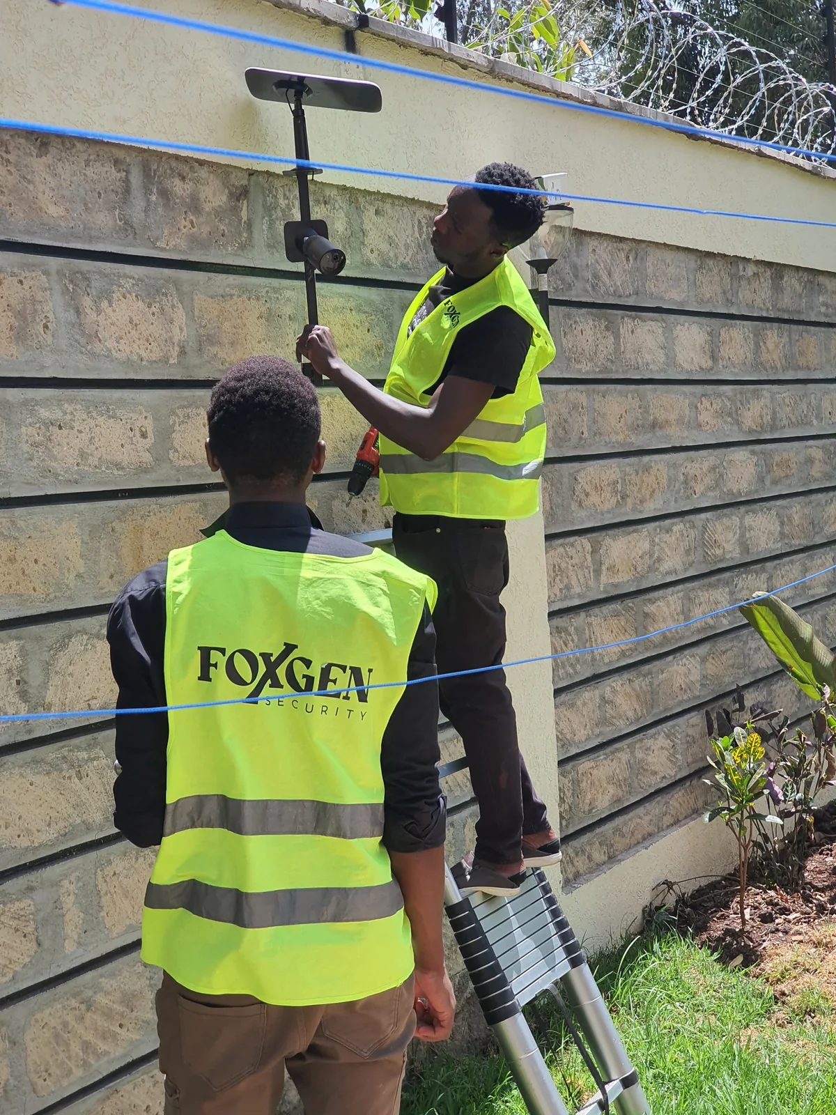 Two Foxgen technicians working on a boundary wall with electric fencing